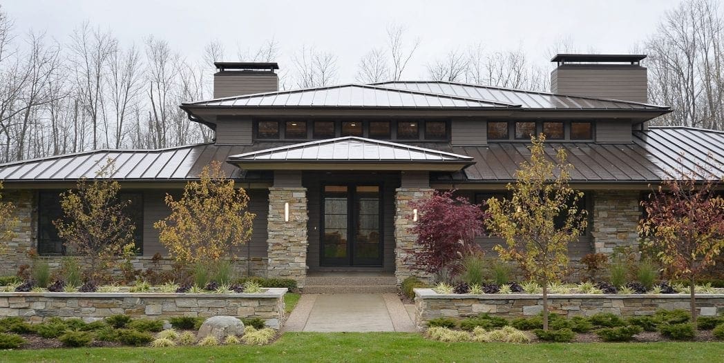 Curb View of Residential Home with Smokey Gold Pillars, Wainscoting, and Landscape Wall